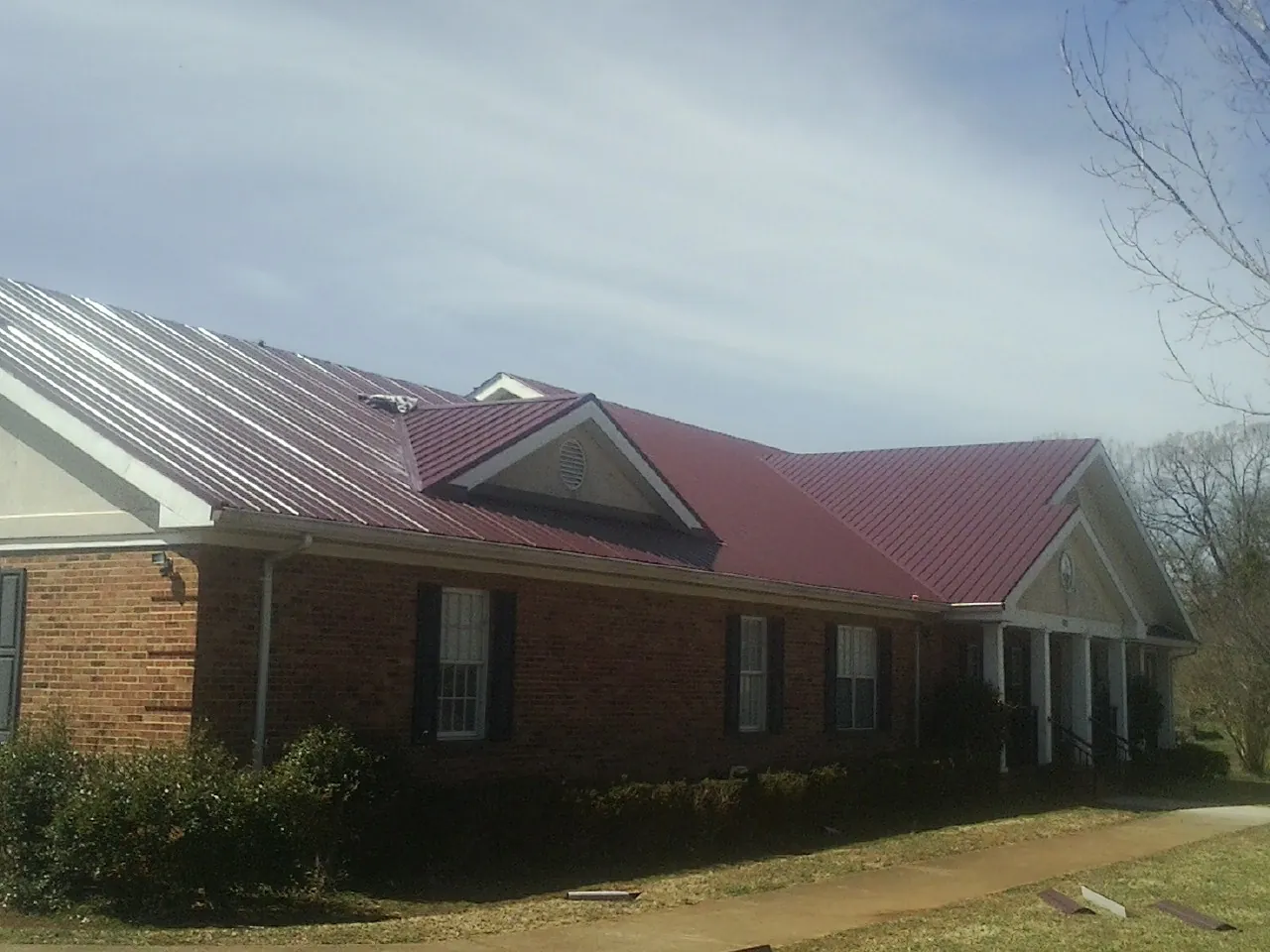 Red metal roof with gabled entries on a long brick building, from a Hail Damage Roof Repair job in Beulah