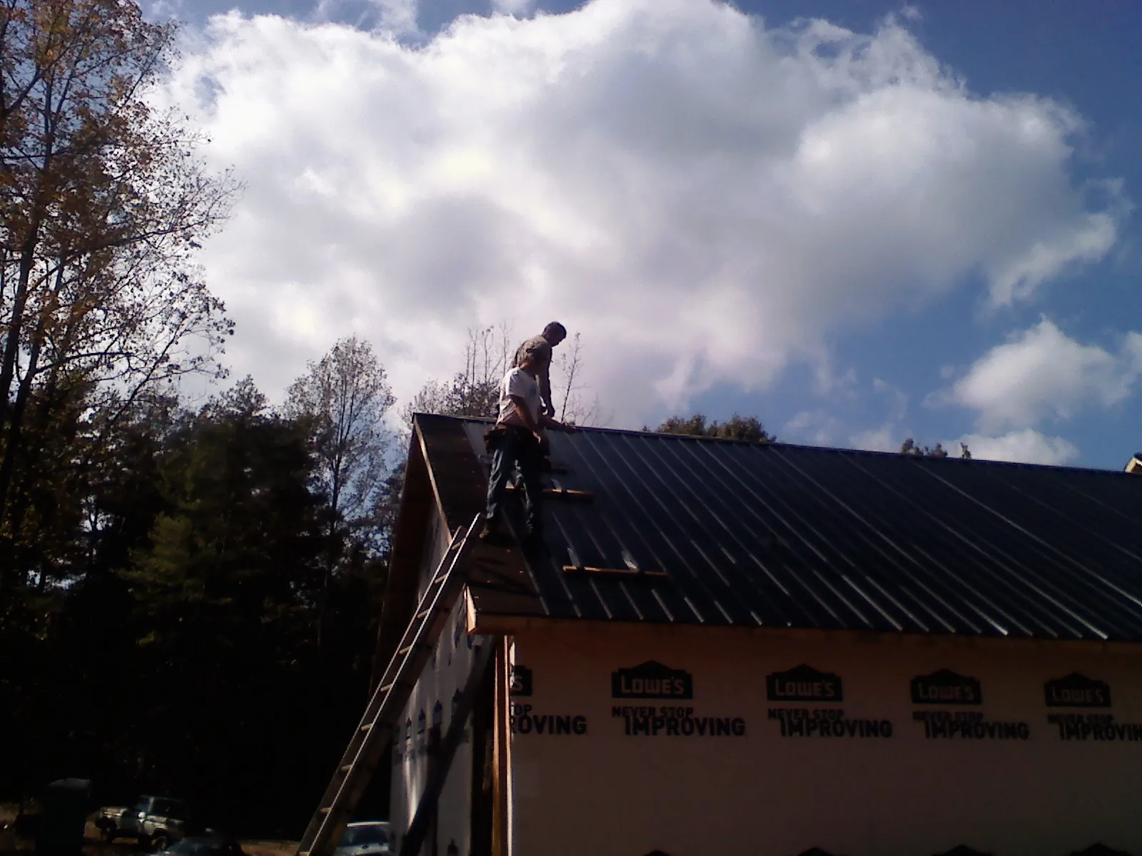 Roofer fastening dark metal panels high against a cloudy sky, from a Roof Inspection job in Beulah