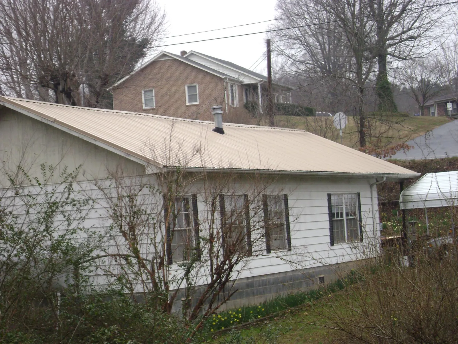 Tan metal roof on a white sided house set into a hillside — Commercial Roofing by Roofing Brothers in Beulah